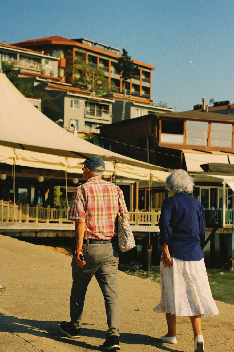A retired couple walking together along a sunlit waterfront